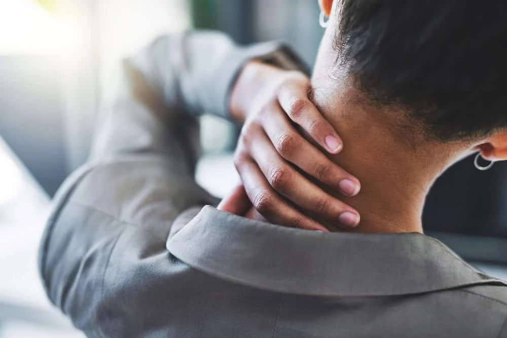 A woman experiencing neck pain holds the back of her neck with one hand, reflecting discomfort and the need for professional neck pain treatment in NYC.