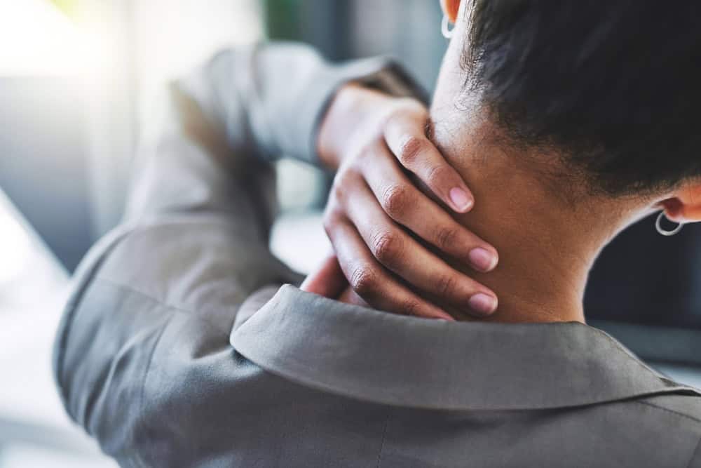 A woman experiencing neck pain holds the back of her neck with one hand, reflecting discomfort and the need for professional neck pain treatment in NYC.
