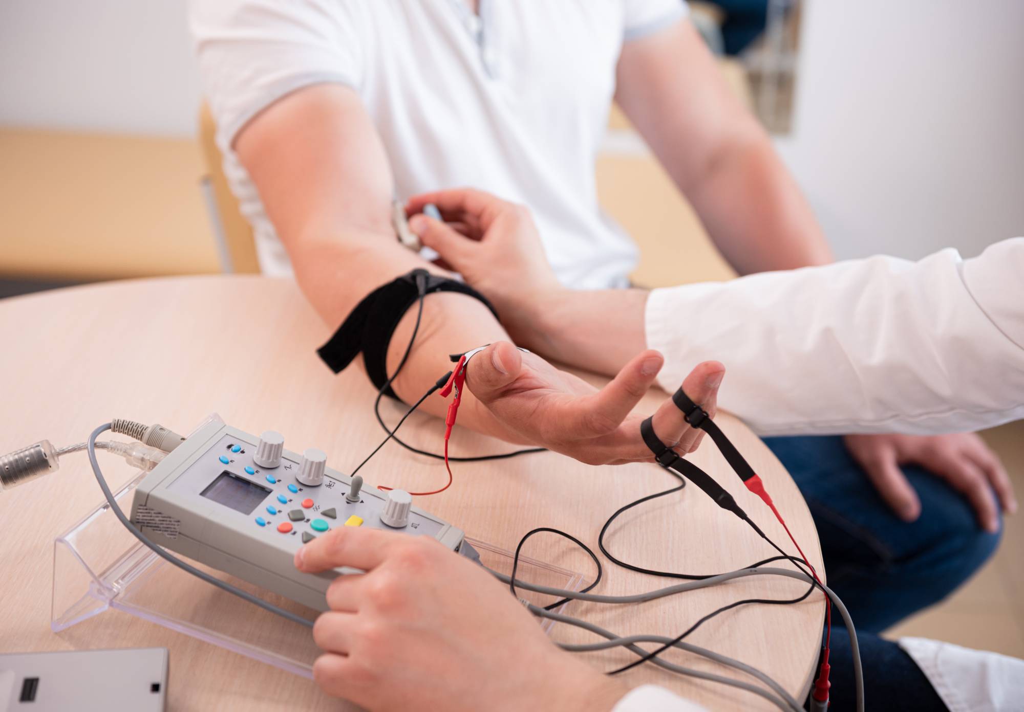 A person in a white shirt has electrodes attached to their arm, while another person in a lab coat operates a polygraph machine on a table, indicating a lie detector test in progress.