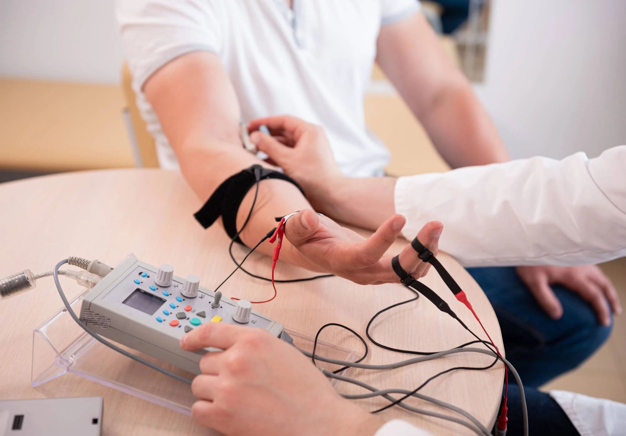 A person in a white shirt has electrodes attached to their arm, while another person in a lab coat operates a polygraph machine on a table, indicating a lie detector test in progress.